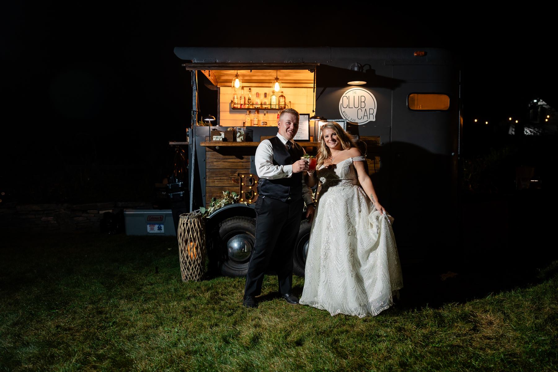 Newlyweds toasting in front of the Club Car mobile bar trailer at night