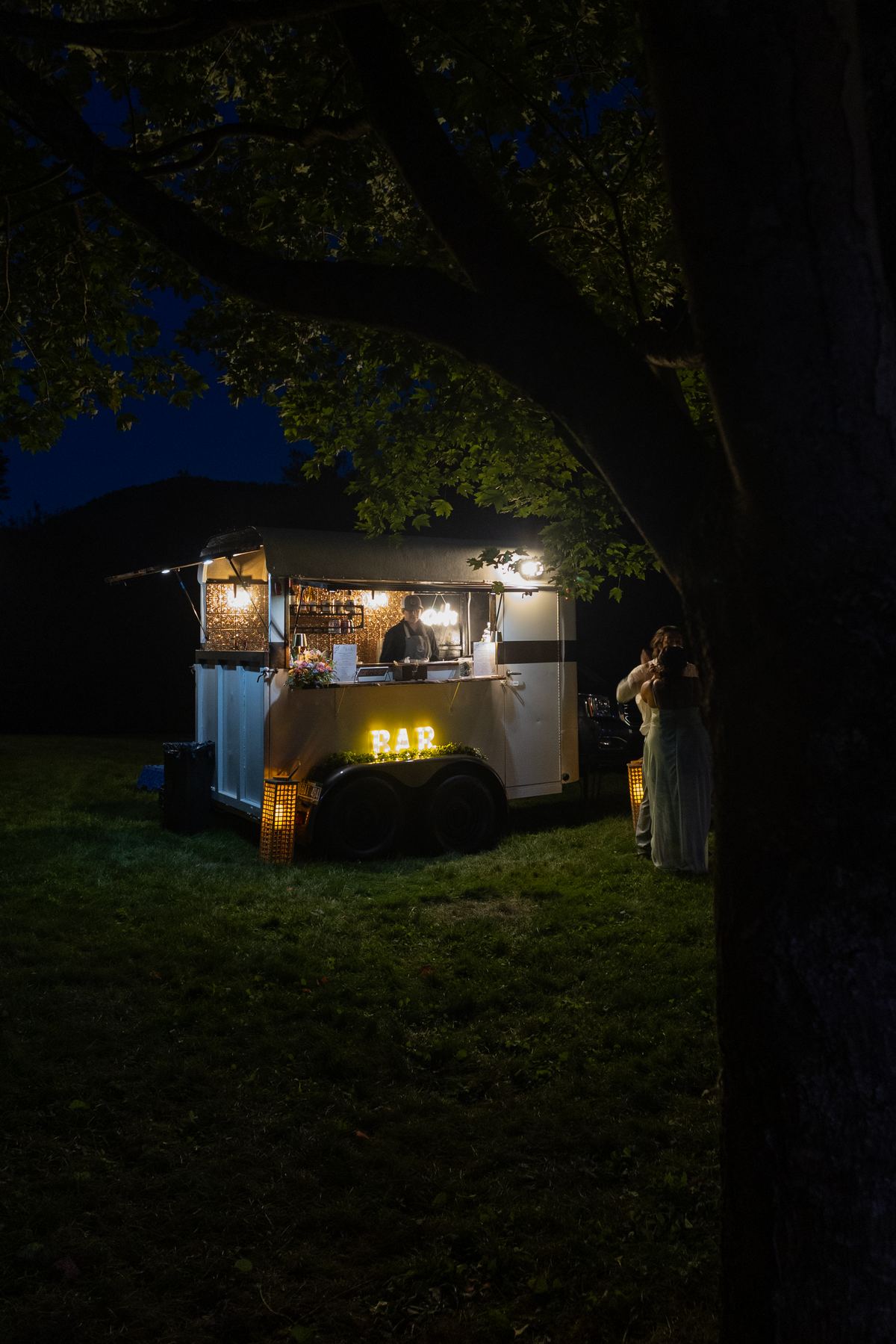 The Parlor Car mobile bar lit up under a tree at night