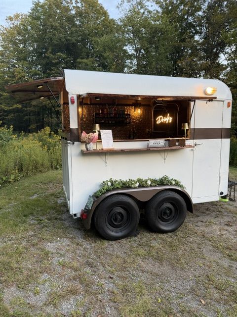 The Parlor Car mobile bar trailer set up outdoors with string lights and a neon sign